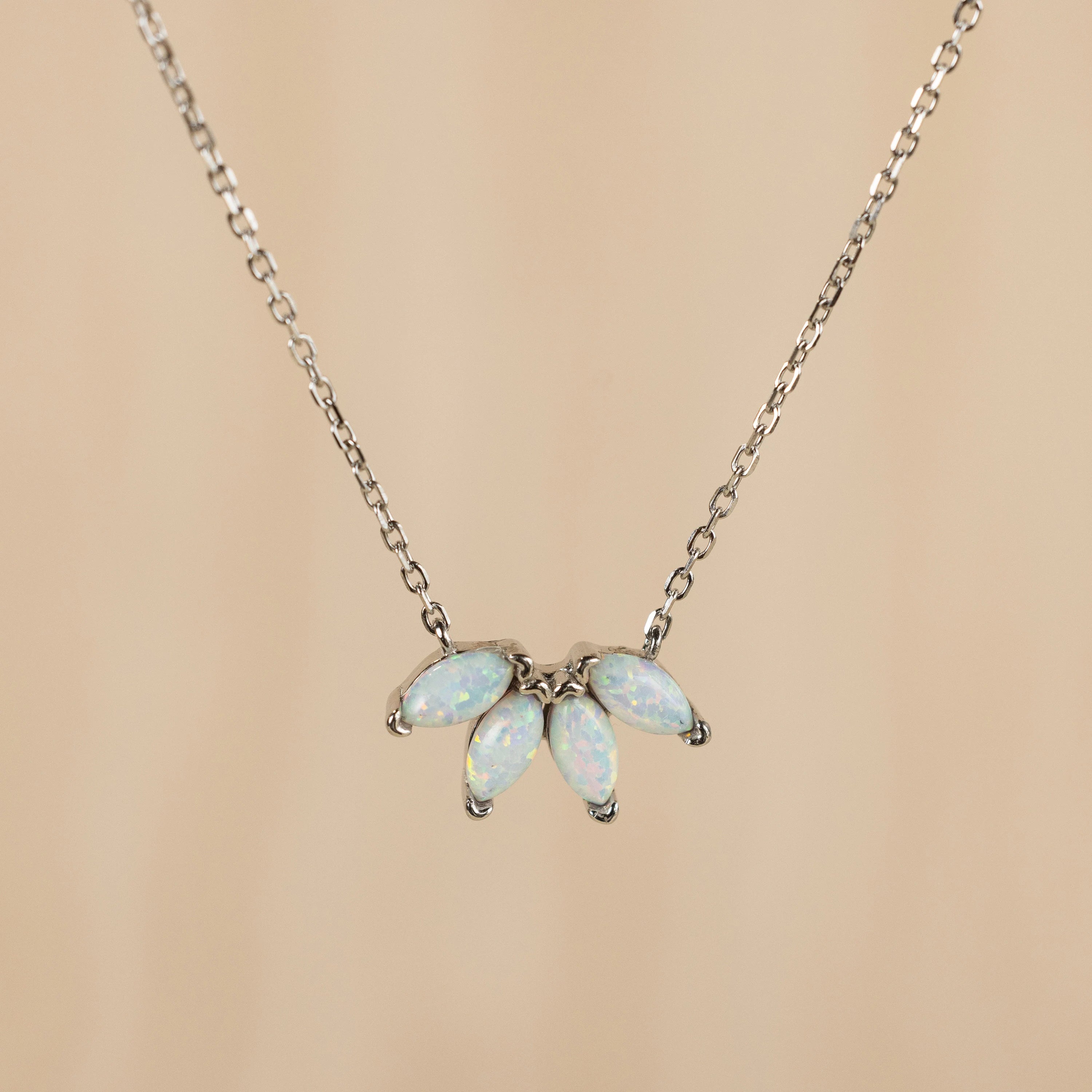 The White Opal Marquise Necklace features five marquise opal stones in a fan shape on a silver chain, adding elegance to your gemstone collection. Shown against a beige background.