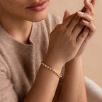 A woman wearing a beige sweater showcases the Pear Diamond Tennis Bracelet, featuring pear-cut diamonds, as her hands are gently clasped near her face.