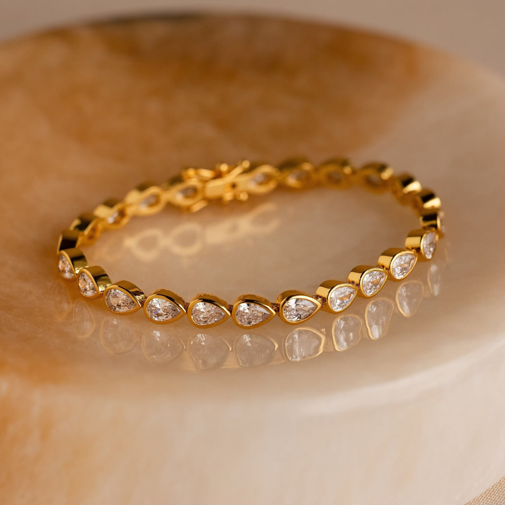 The Pear Diamond Tennis Bracelet, featuring teardrop-shaped white stones, is elegantly displayed on a polished marble surface.