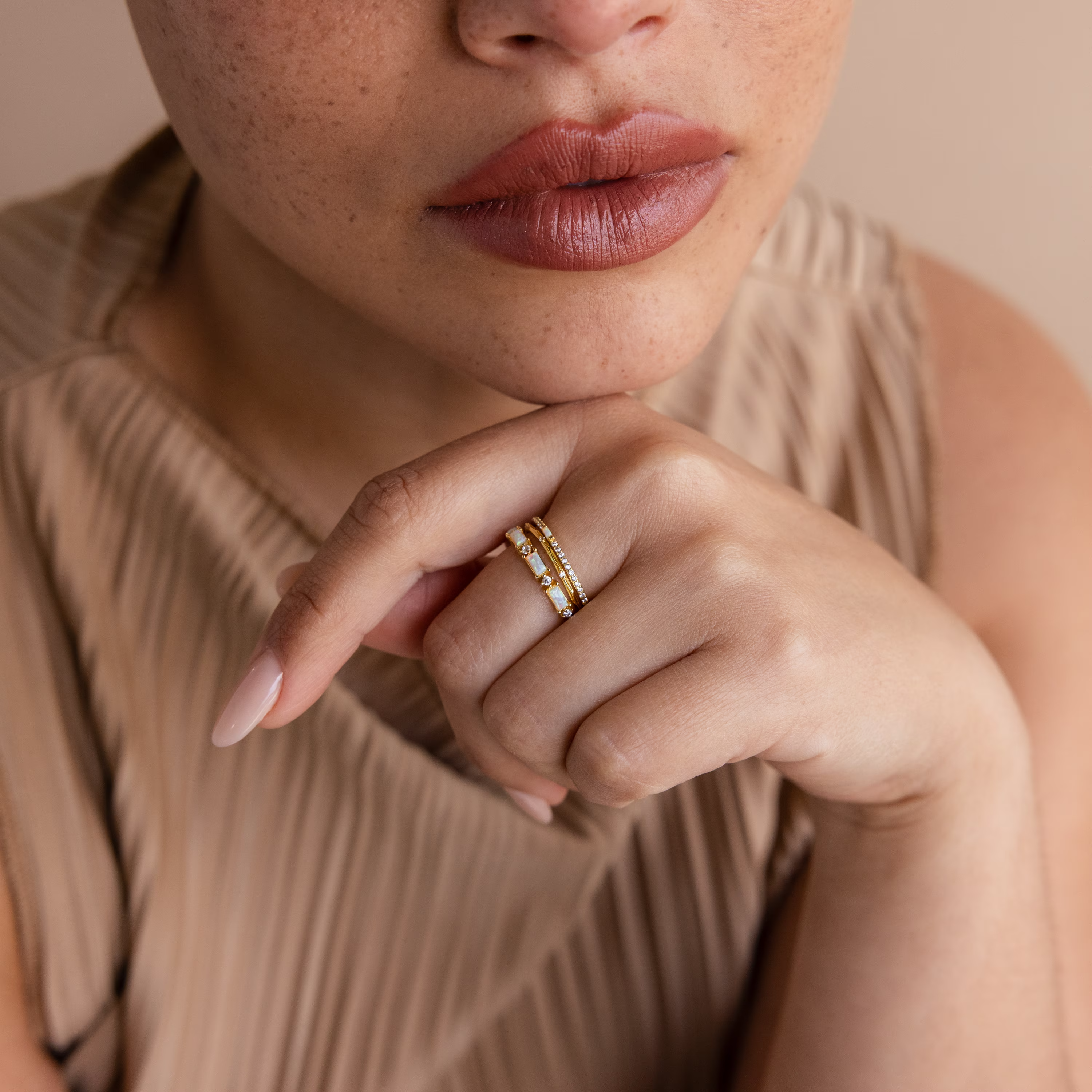 A woman with freckles wears a pleated beige top and the Pave Opal Ring Set, featuring timeless design and diamonds, on her finger near her lips.