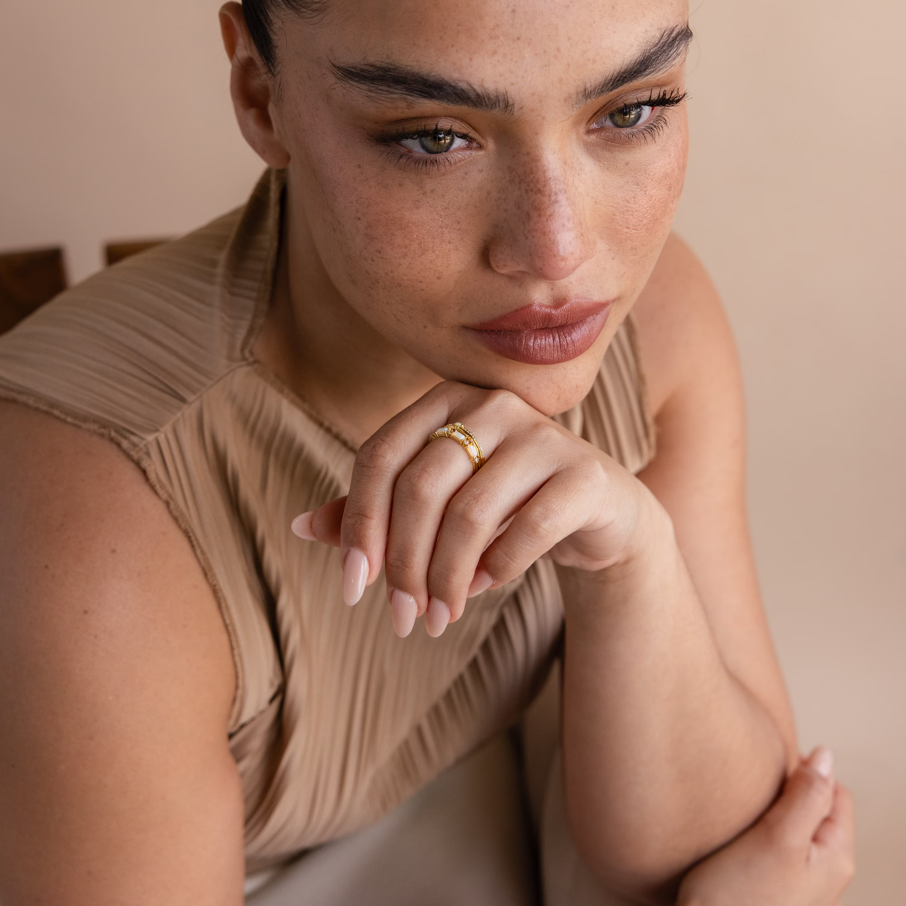 A woman with freckles rests her chin on her hand, wearing a Pave Opal Ring Set in 18K Gold—a timeless design that captures quiet elegance.