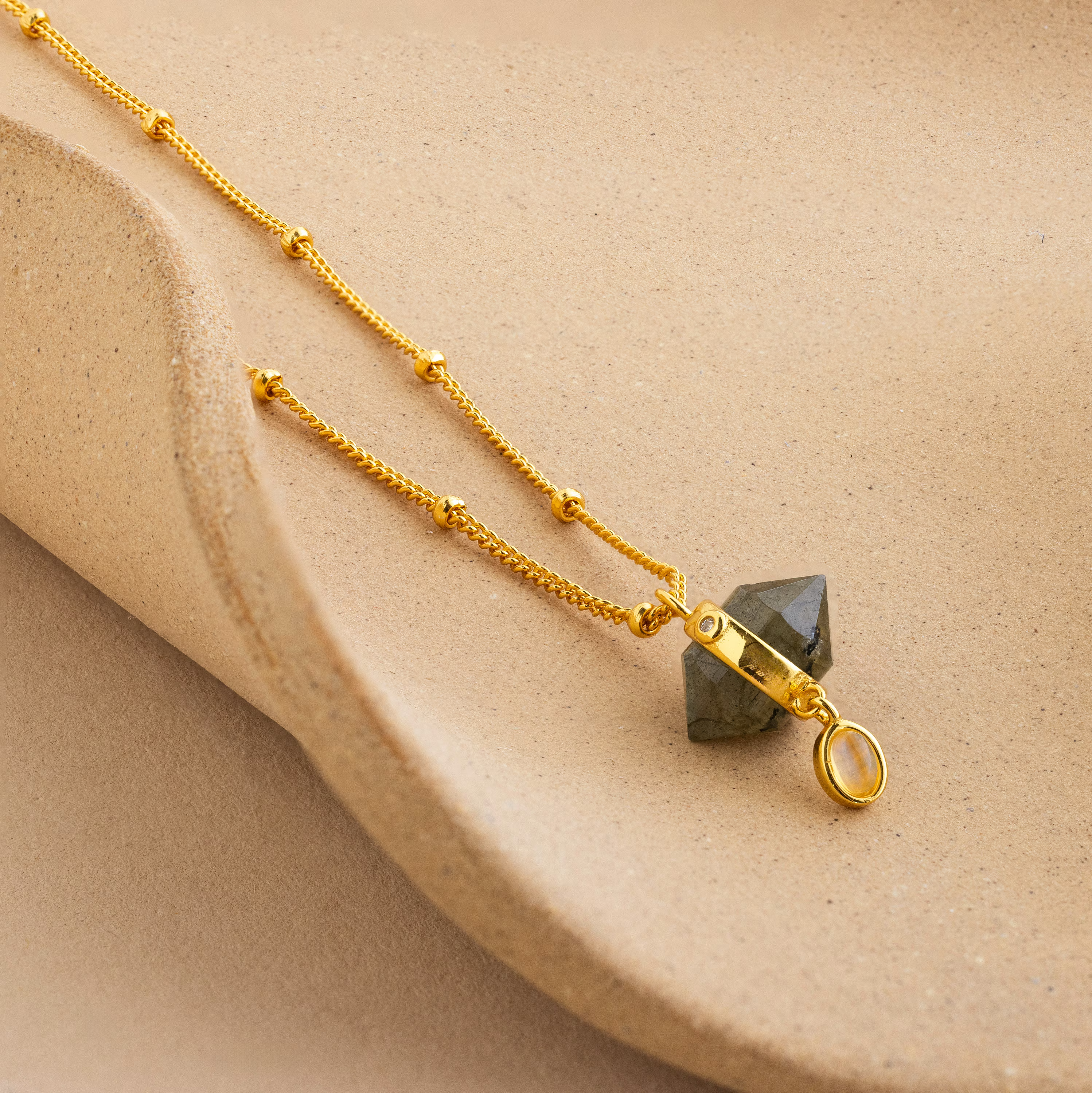 Labradorite & Moonstone Drop Necklace featuring a geometric pendant, elegantly displayed on a textured beige surface.