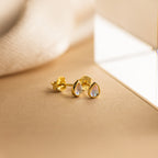 The Pear Moonstone Studs, featuring iridescent stones in a gold teardrop design, radiate celestial charm and elegance against a soft beige background.