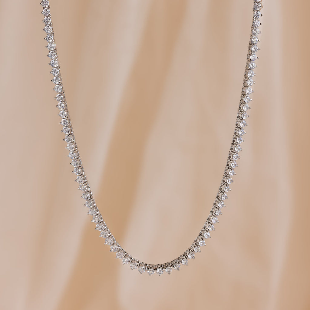 The 3 Prong Tennis Necklace, adorned with sparkling diamonds, is displayed against a soft beige background.