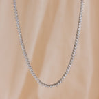 The 3 Prong Tennis Necklace, adorned with sparkling diamonds, is displayed against a soft beige background.