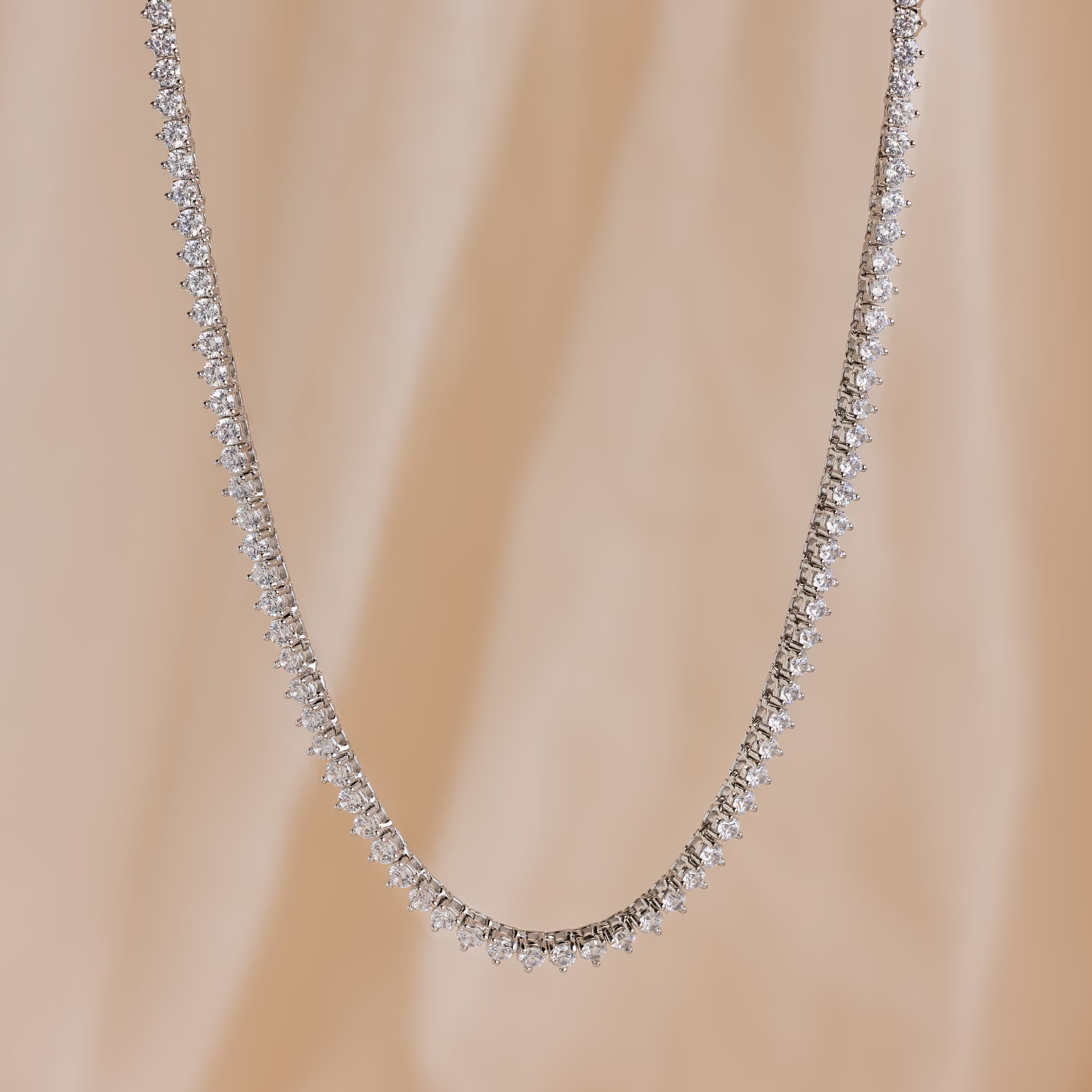 The 3 Prong Tennis Necklace, adorned with sparkling diamonds, is displayed against a soft beige background.