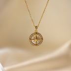 The Pave Pearl Compass Necklace, inspired by nautical jewelry, features a delicate compass pendant and is displayed elegantly on a soft beige satin background.