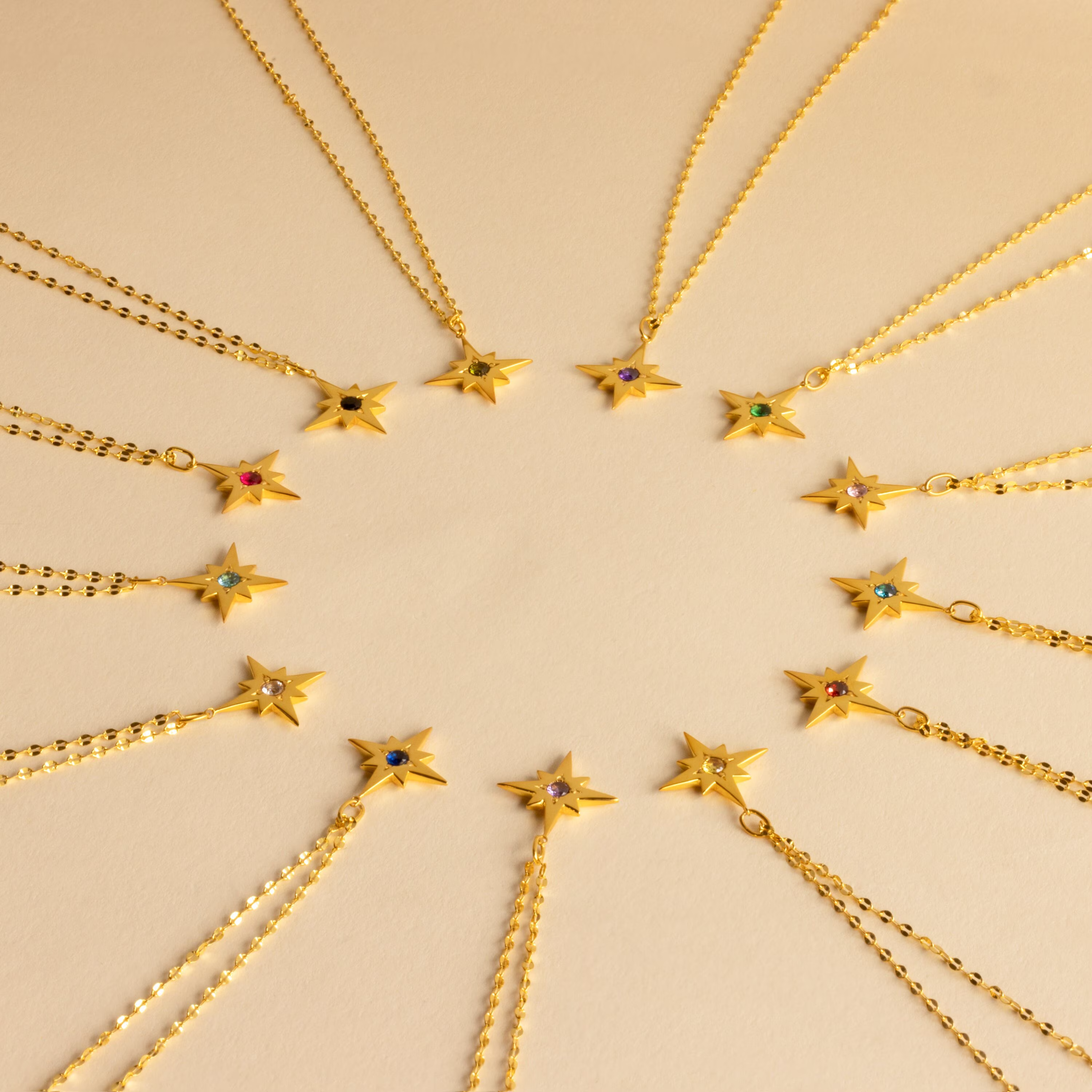 The Star Birthstone Necklace showcases gold star pendants with vibrant gemstones arranged in a circle, set against a beige background—an ideal personalized gift.