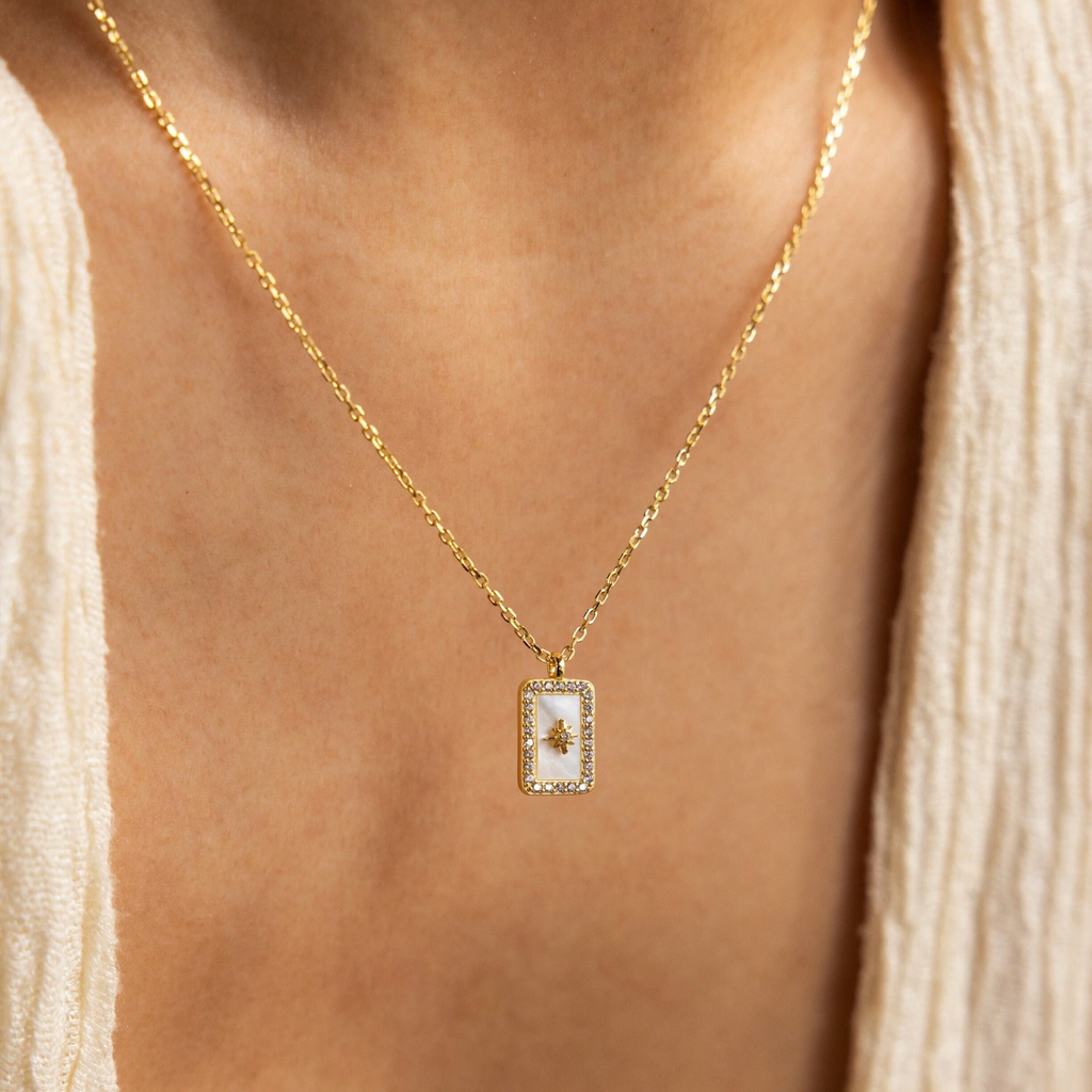 Pave Pearl North Star Necklace—a gold piece featuring a delicate rectangular pendant with a tree design, styled over a cream textured top for an understated celestial jewelry look.