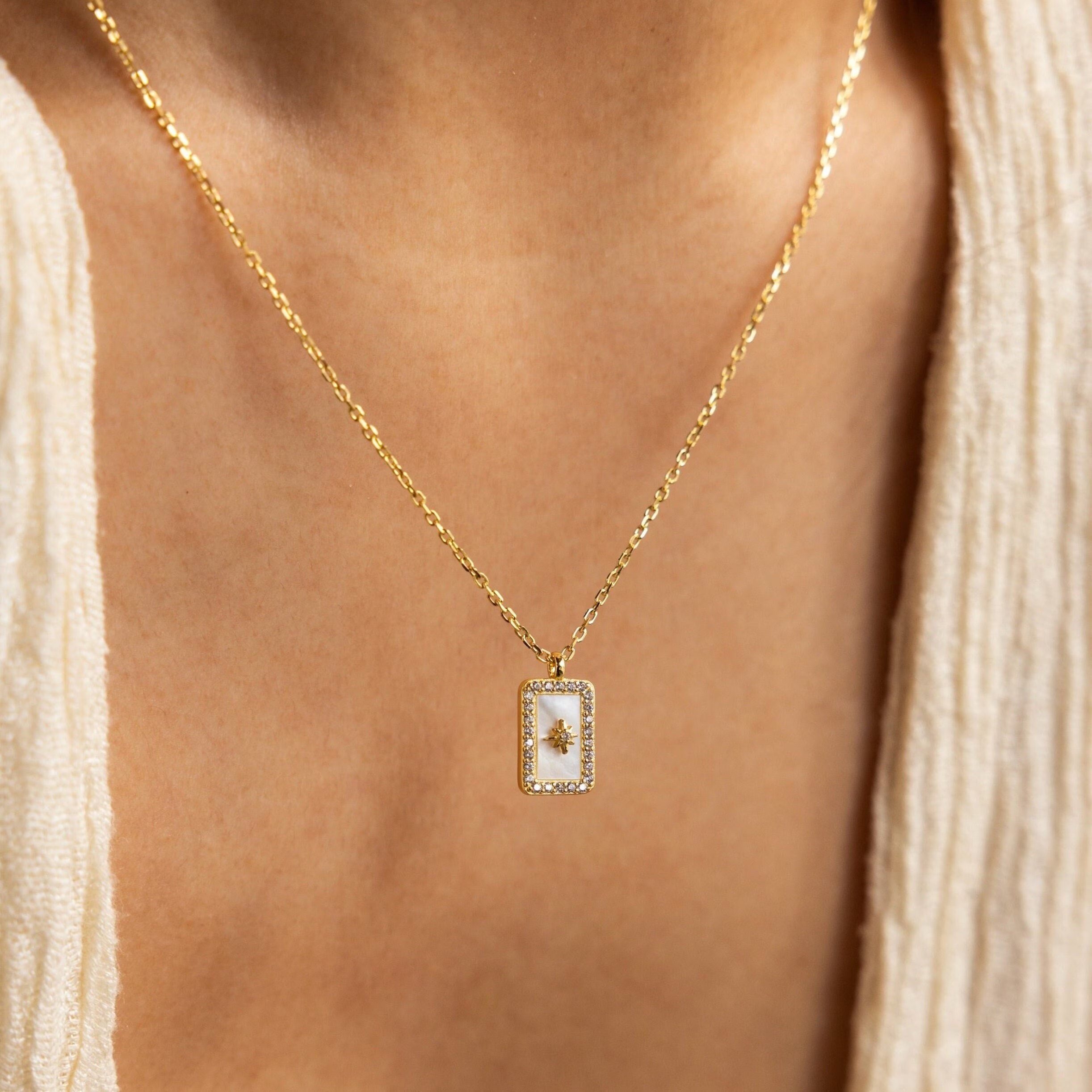 Pave Pearl North Star Necklace—a gold piece featuring a delicate rectangular pendant with a tree design, styled over a cream textured top for an understated celestial jewelry look.