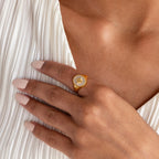 A hand with manicured nails showcases the North Star Signet Ring, making a statement on a pleated white top.