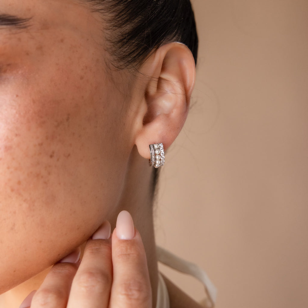 A woman displays Diamond Pearl Stacked Hoops on her ear, hand near her chin, set against a neutral background—these hoops offer an elegant bridal jewelry option.