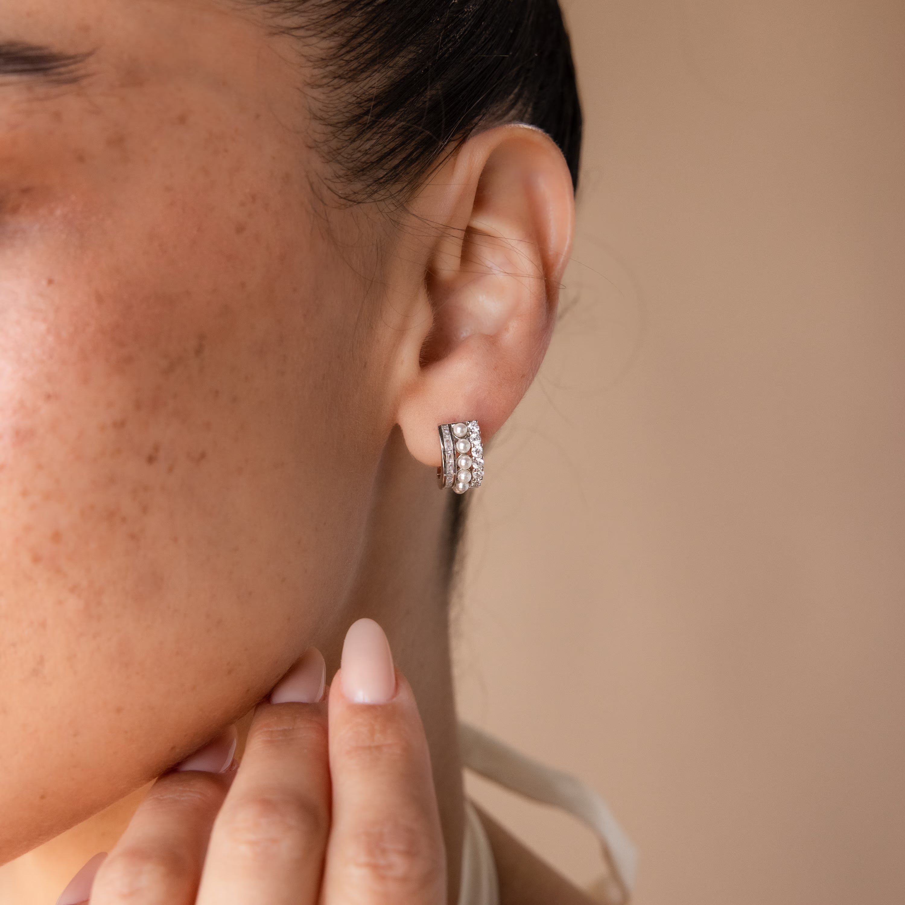 A woman displays Diamond Pearl Stacked Hoops on her ear, hand near her chin, set against a neutral background—these hoops offer an elegant bridal jewelry option.
