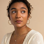 Woman with curly hair wearing Large Twisted Hoops and layered necklaces, gazing to the side—these earrings are the perfect summer accessory to elevate her effortless style.
