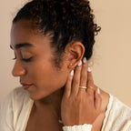 A woman with curly hair and patterned nails, eyes closed, touches her ear adorned with gold Opal Threader Huggies celestial jewelry.