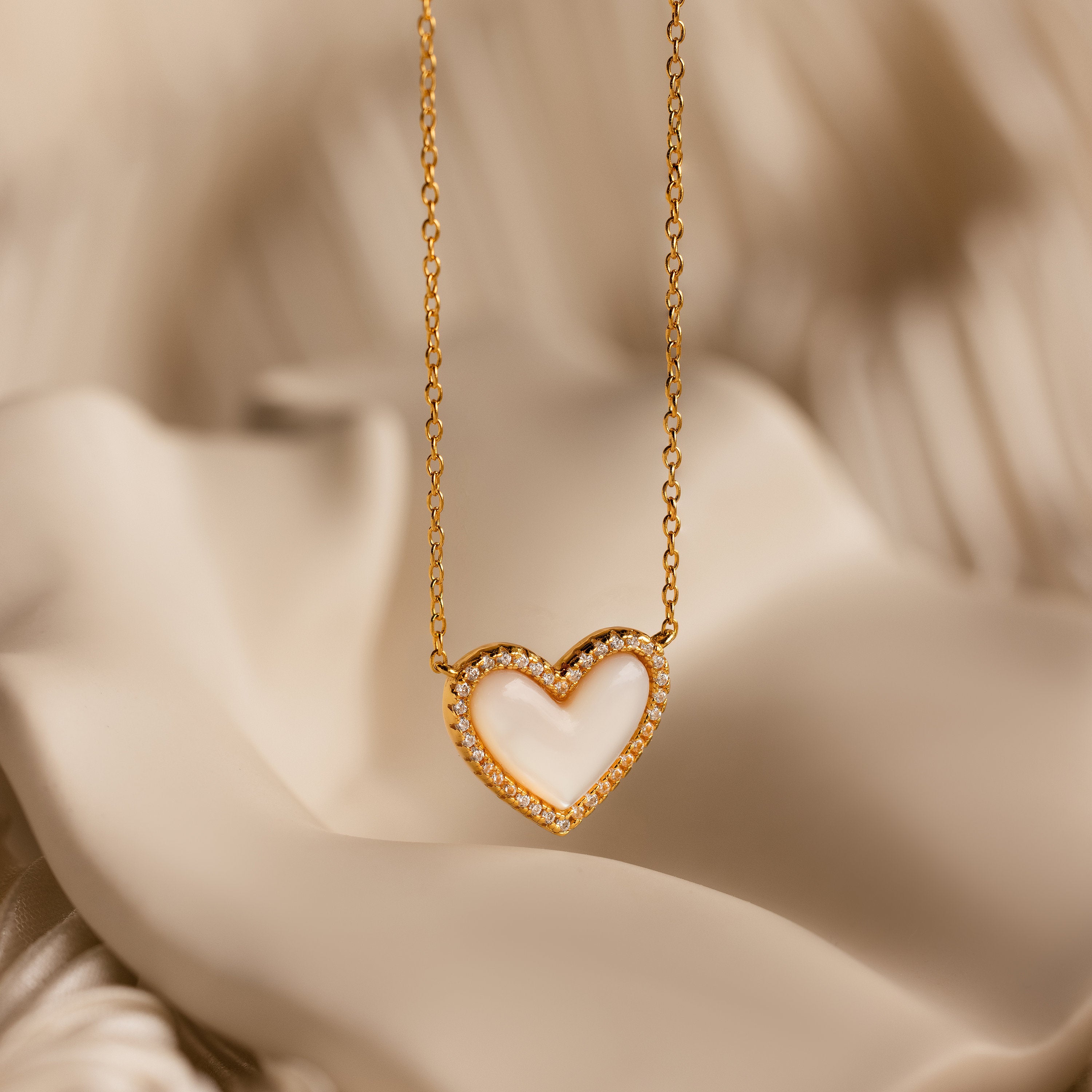Pave Mother of Pearl Heart Necklace with small diamonds, vintage-inspired heart design, showcased on soft cream-colored fabric.