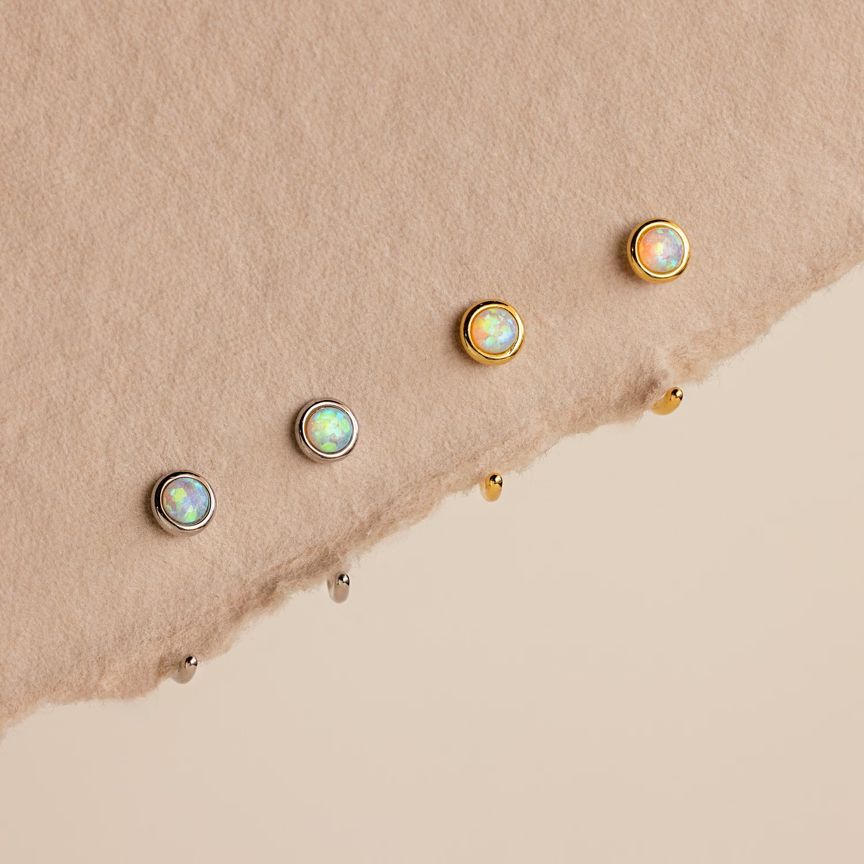 Two silver and two gold Opal Threader Huggies are displayed on a textured beige surface—an elegant set perfect for lovers of celestial jewelry and opal earrings.