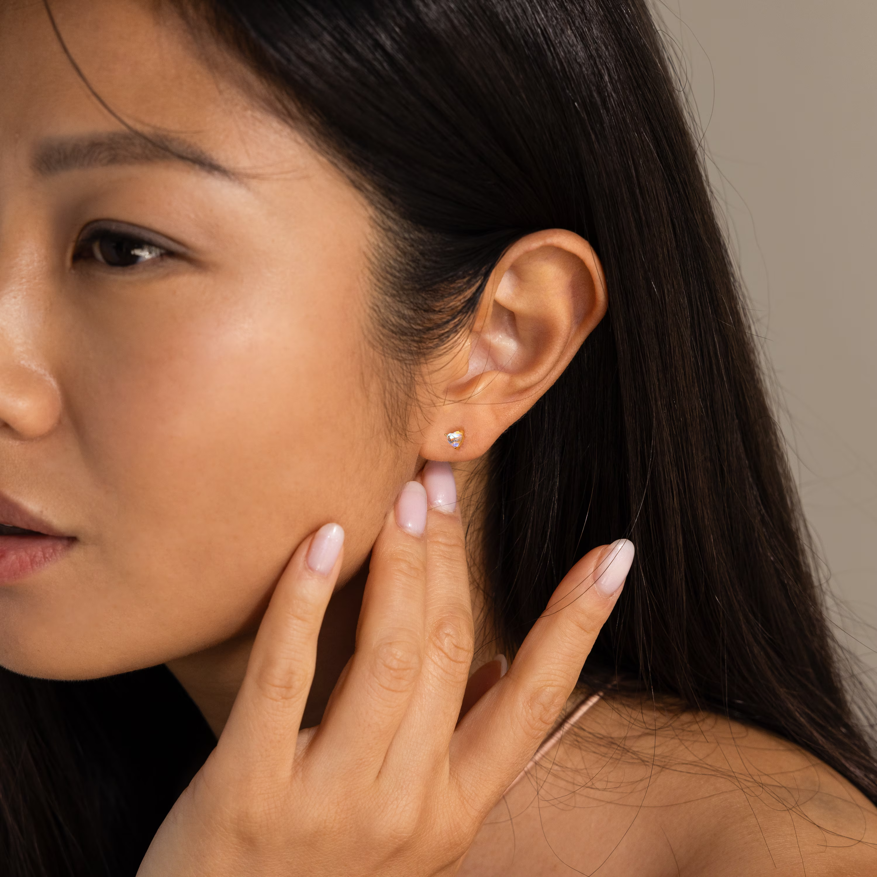 A woman touches her ear, showcasing Moonstone Heart Studs—dainty earrings with heart-shaped moonstones.