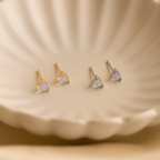 Two pairs of Moonstone Heart Studs, in both gold and silver finishes, are displayed on a cream scalloped dish.