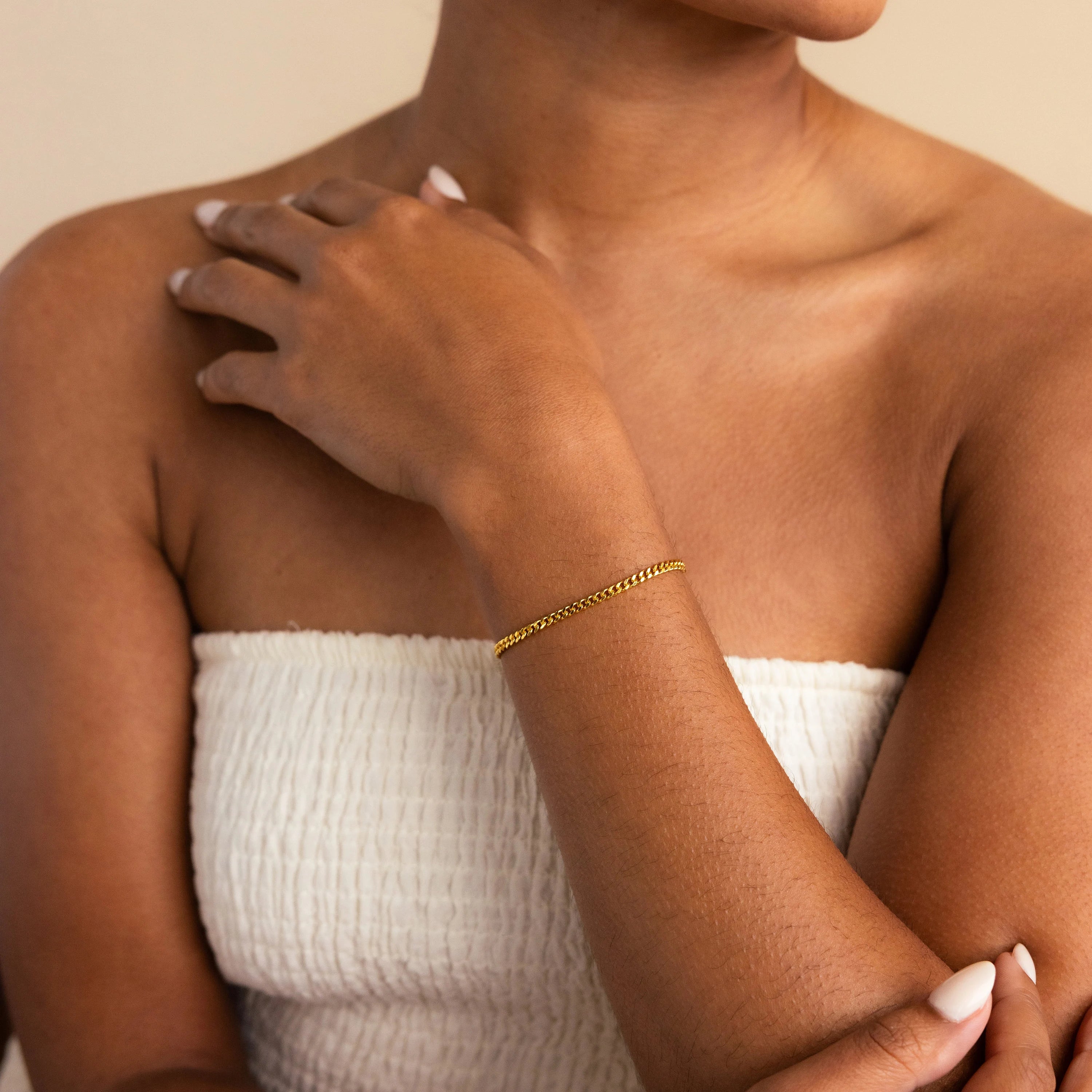 A woman in a white textured top showcases minimal style with the Curb Chain Bracelet, her hand resting elegantly on her shoulder.