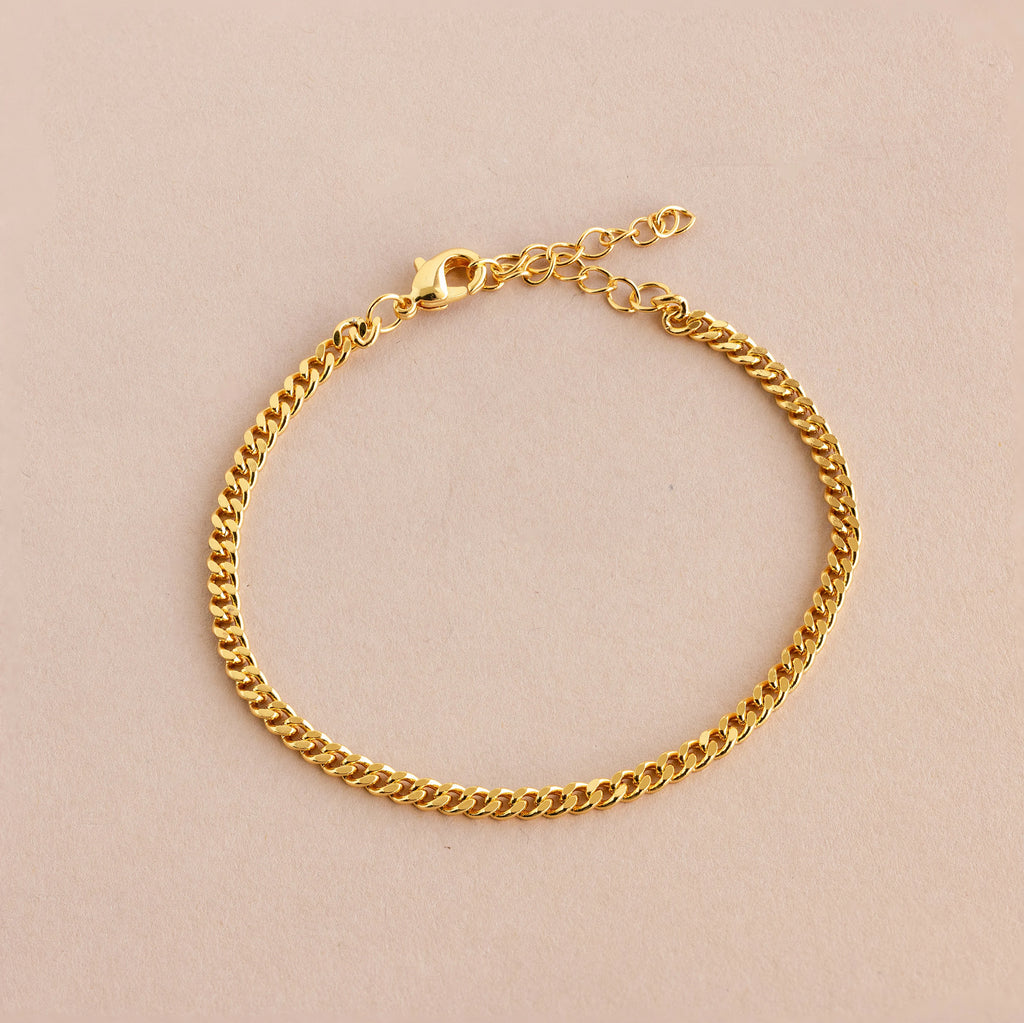 The Curb Chain Bracelet shines with minimal elegance, featuring a lobster clasp and extender chain for easy layering. Shown on a light beige background.