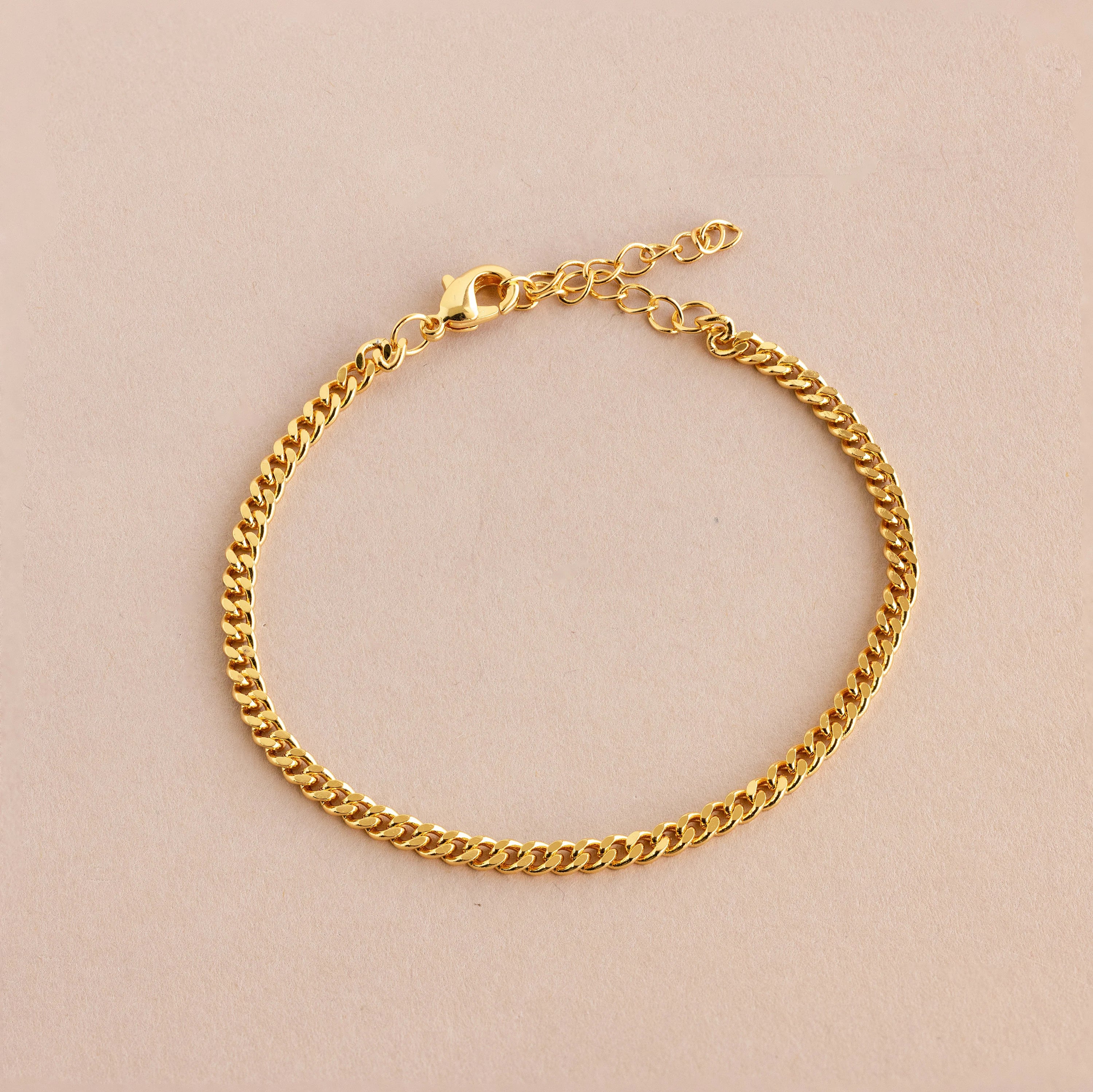 The Curb Chain Bracelet shines with minimal elegance, featuring a lobster clasp and extender chain for easy layering. Shown on a light beige background.
