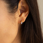 Close-up of a woman's ear wearing Moonstone Heart Huggies—small gold hoops featuring heart-shaped moonstones and a clear gemstone accent.