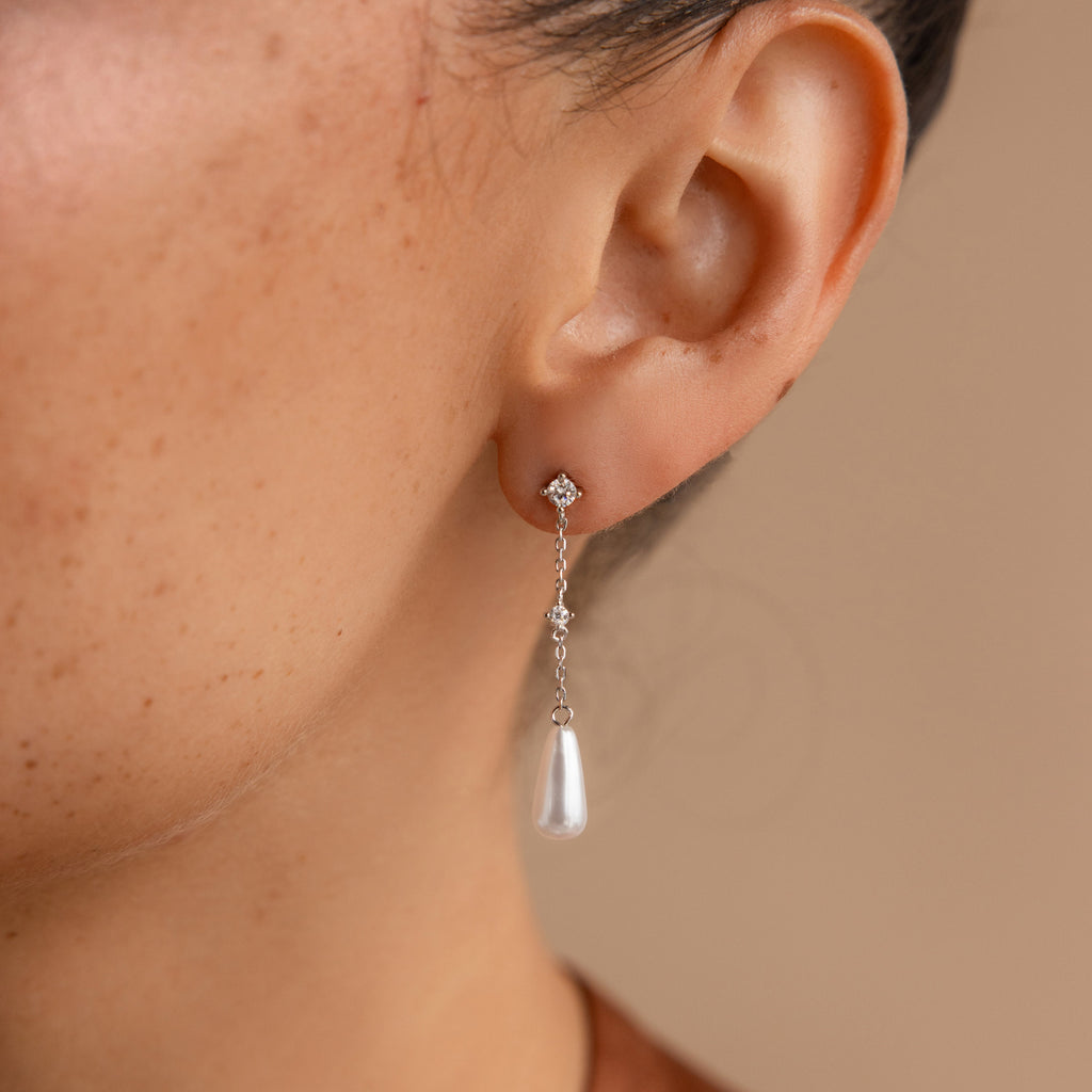 A woman's ear wearing Diamond Pearl Chain Earrings, which showcase a delicate diamond stud paired with an elegant pearl teardrop charm.