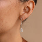 A woman's ear wearing Diamond Pearl Chain Earrings, which showcase a delicate diamond stud paired with an elegant pearl teardrop charm.