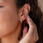 A woman fastens her Clear Moonstone Huggies, adding a refined touch to her look.