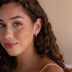 Woman with long curly hair wears Clear Moonstone Huggies, smiling softly and looking at the camera.