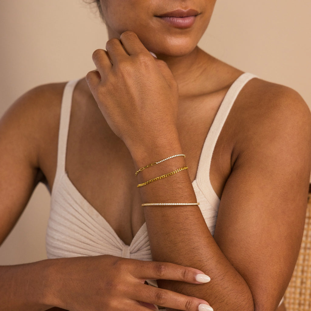 Woman in a beige top wears three delicate gold and silver bracelets, including the Classic Diamond Tennis Bangle adorned with pavé stones, on her left wrist.