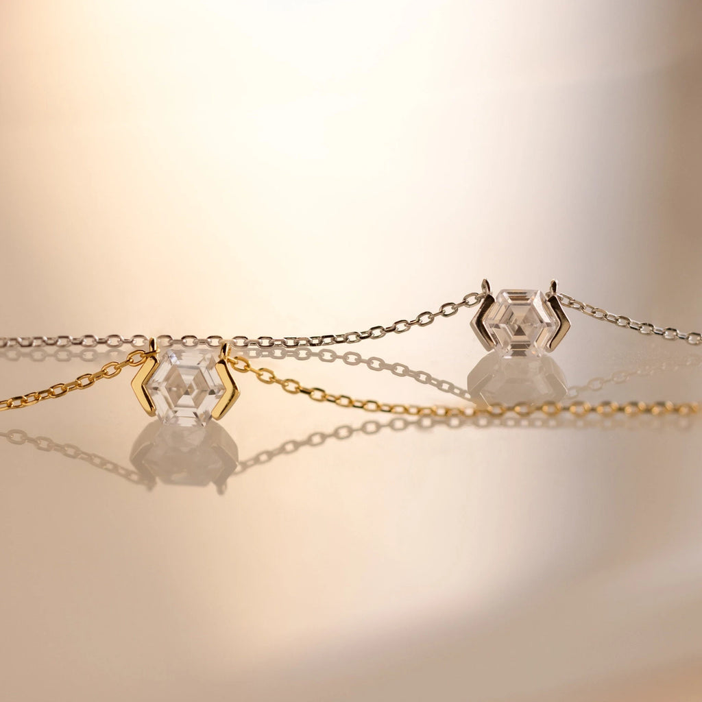 Two delicate necklaces with hexagonal crystal pendants—one on a gold chain and one on a silver—offer modern elegance reminiscent of the Encased Hexagon Diamond Necklace in a half-bezel setting.