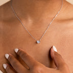 A hand touches the collarbone while wearing the Encased Hexagon Diamond Necklace, featuring a delicate hexagon diamond in a half-bezel setting for a modern, sophisticated look.