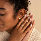 Woman with curly hair wears Opal Signet Huggies and rings, gently touching her face with closed eyes.