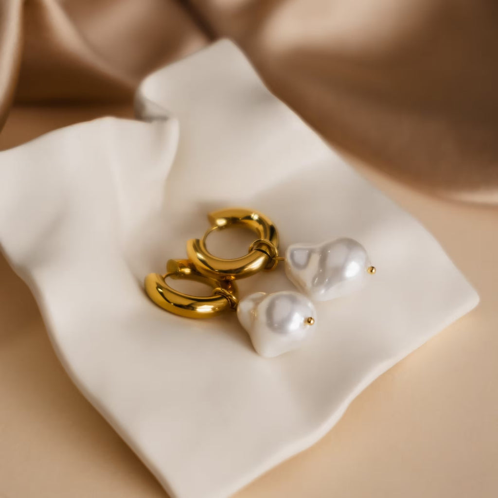 Baroque Pearl Earrings Set—gold hoops with dangling white pearls—rests elegantly on cream-colored fabric.