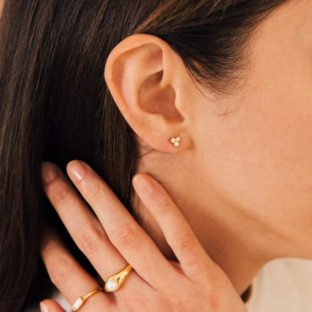 Close-up of a woman's ear wearing a Baroque Pearl Earrings Set, featuring a small flower-shaped stud and her hand adorned with a gold pearl ring, all styled with delicate baroque pearls.