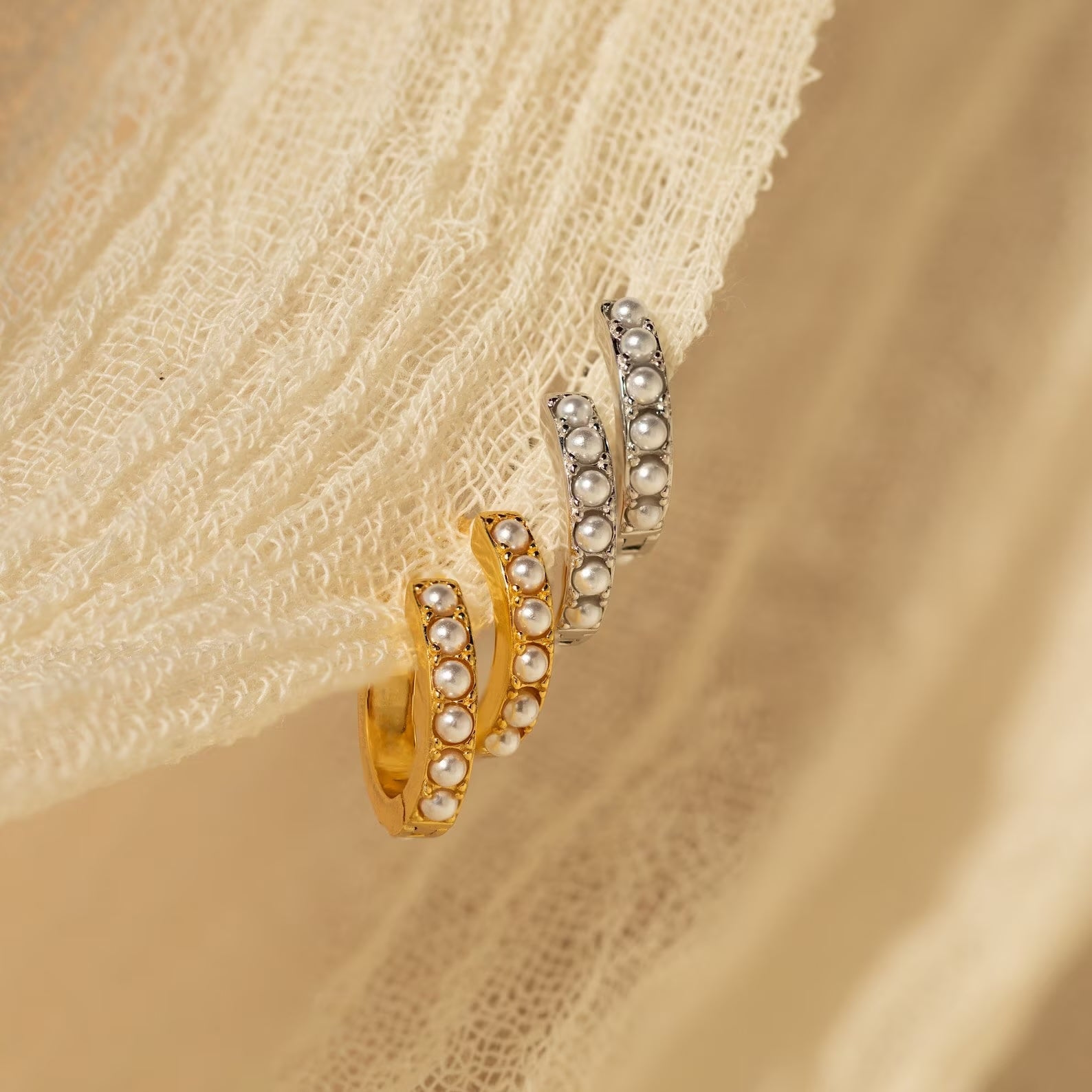 The Baroque Pearl Earrings Set features gold and silver earrings with pearl accents, displayed on cream-textured fabric.