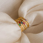 A stack of gold rings with colorful gemstones, featuring the Marquise Bezel Birthstone Ring, displayed on cream-colored fabric.
