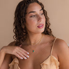 A woman with curly hair wearing a peach ruffled top and layered gold necklaces, featuring the Turquoise Pendant Necklace, looks to the side.