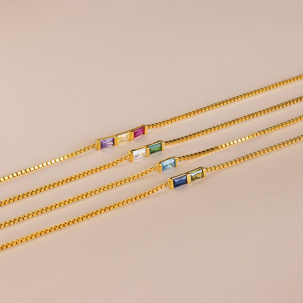 Four Multiple Baguette Birthstone Bracelets with gold box chains and two colorful rectangular gemstone charms each are displayed on a beige background—perfect as a custom birthstone bracelet gift.