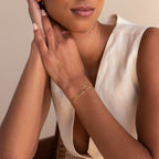 Woman in a sleeveless cream top wears the Multiple Baguette Birthstone Bracelet and a gold ring with pink stones, hands clasped near her face.