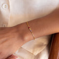 The Multiple Baguette Birthstone Bracelet features delicate gold with colorful rectangular stones, elegantly adorning the wrist against a cream blouse.