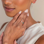 A woman in a sleeveless top displays her hand adorned with the Duo Heart Birthstone Ring—two heart-shaped gemstones set on a gold band, offering a unique and personalized touch.