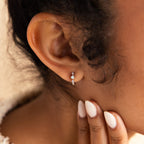 Close-up of a woman's ear wearing a single silver huggie earring adorned with a central opal flanked by two small diamonds, paired with neatly manicured nails gently touching the side of her neck.