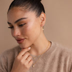 A woman rests her hand on her chin, elegantly showcasing her Pave Opal Star Huggies.