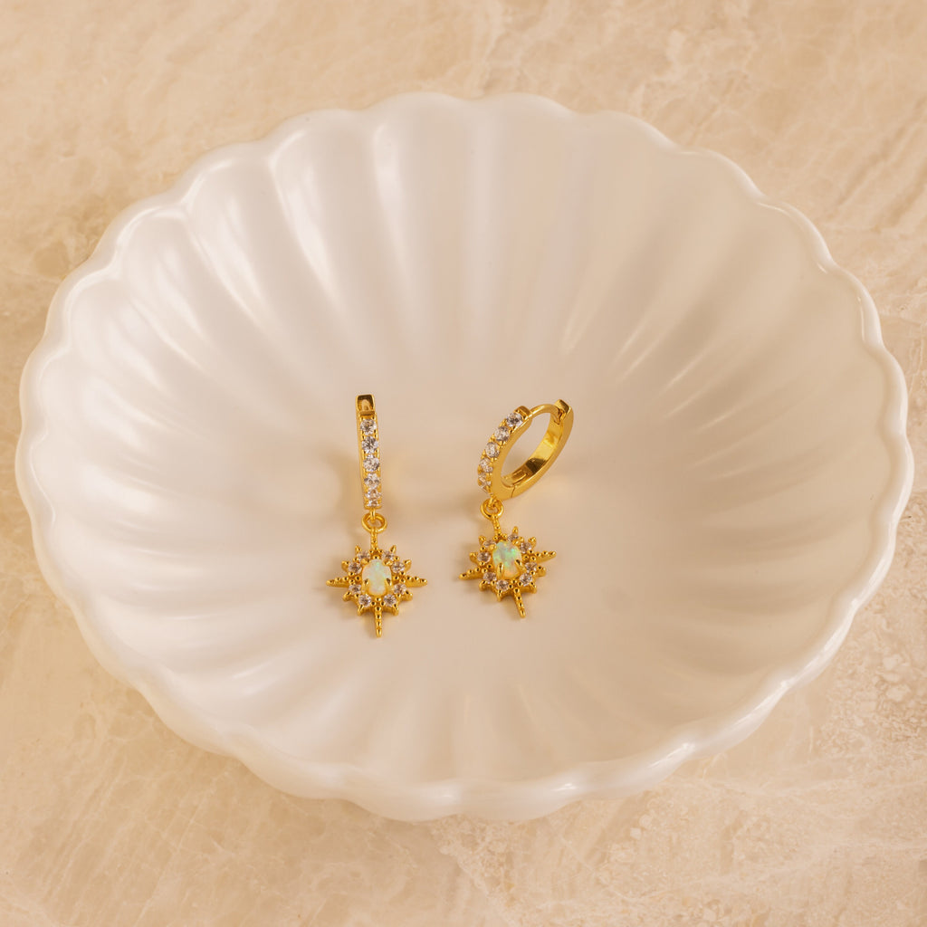 Pave Opal Star Huggies are displayed on a white scalloped dish, adding a sparkling touch to the beige surface.