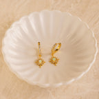 Pave Opal Star Huggies are displayed on a white scalloped dish, adding a sparkling touch to the beige surface.