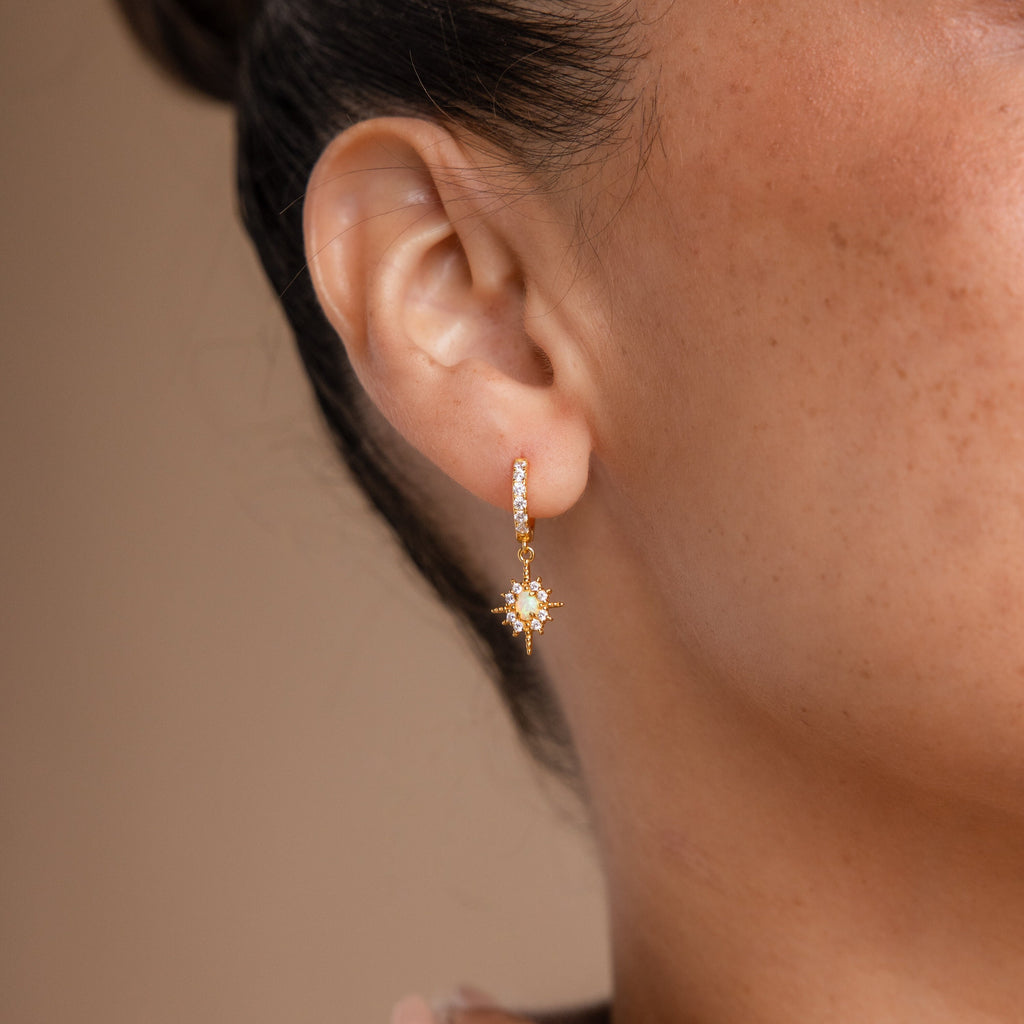 Close-up of a woman's ear wearing the Pave Opal Star Huggies, featuring a gold star-shaped charm adorned with small white stones and opal accents.