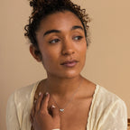 Woman with curly hair wears a cream cardigan and the White Opal Marquise Necklace, gazing slightly to the side against a beige background.